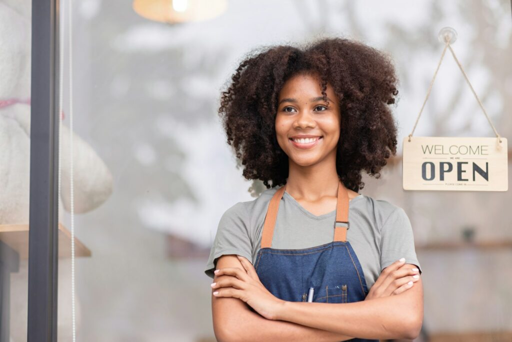 Small business african woman is a waitress in an apron, the owner of the cafe stands at the door